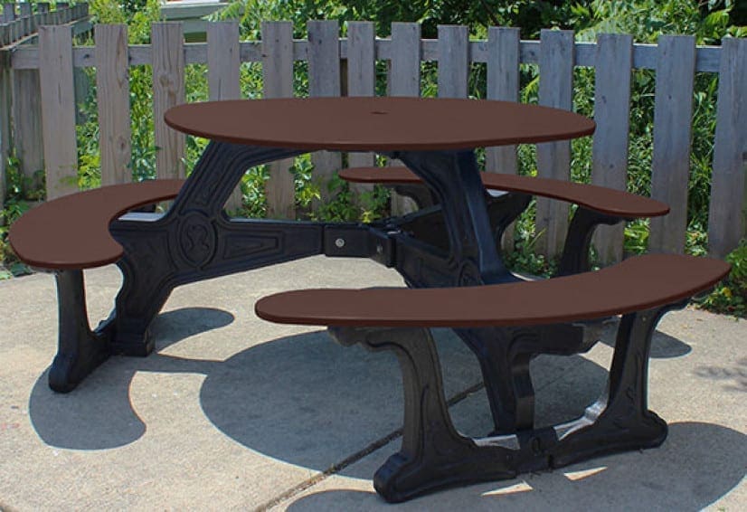 Bodega Outdoor Dining Table placed on a cement patio with a fence in the background. This table is made with our Green-Scapes designer frame which looks like black cast iron, but made from solid, recycled HDPE plastic. The top is made with HDPE sheet plastic. Shown with a black frame and brown top and seat.