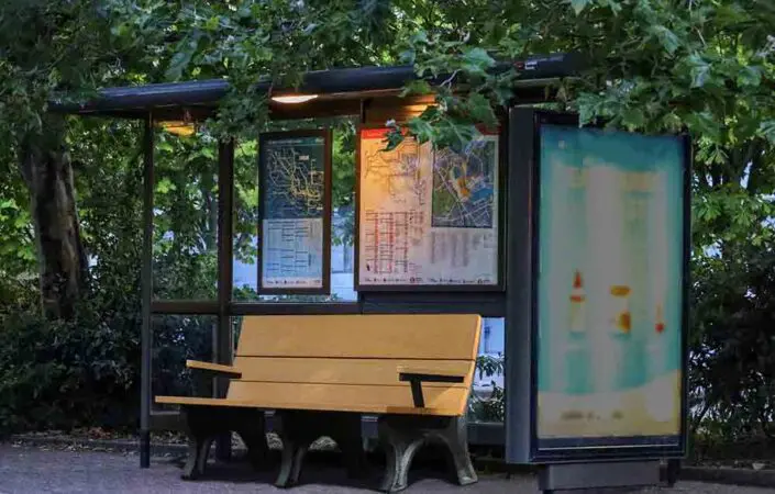 Cedar colored Traditional 6' ADA Backed Park Bench with Arms at a bus stop