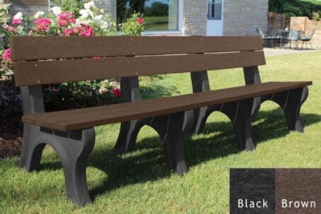 Traditional 8 foot outdoor park bench made out of 100% recycled HDPE plastic. This bench is made with our durable 2"x6" planks and is perfect for parks and trails. Shown with a black frame and brown boards on grass with flowers behind it.