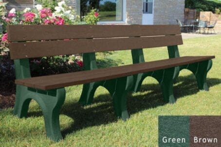 Traditional 8 ft outdoor park bench made out of 100% recycled HDPE plastic. This bench is made with our durable 2"x6" planks and is perfect for parks and trails. Shown with a green frame and brown boards on grass with flowers behind it.